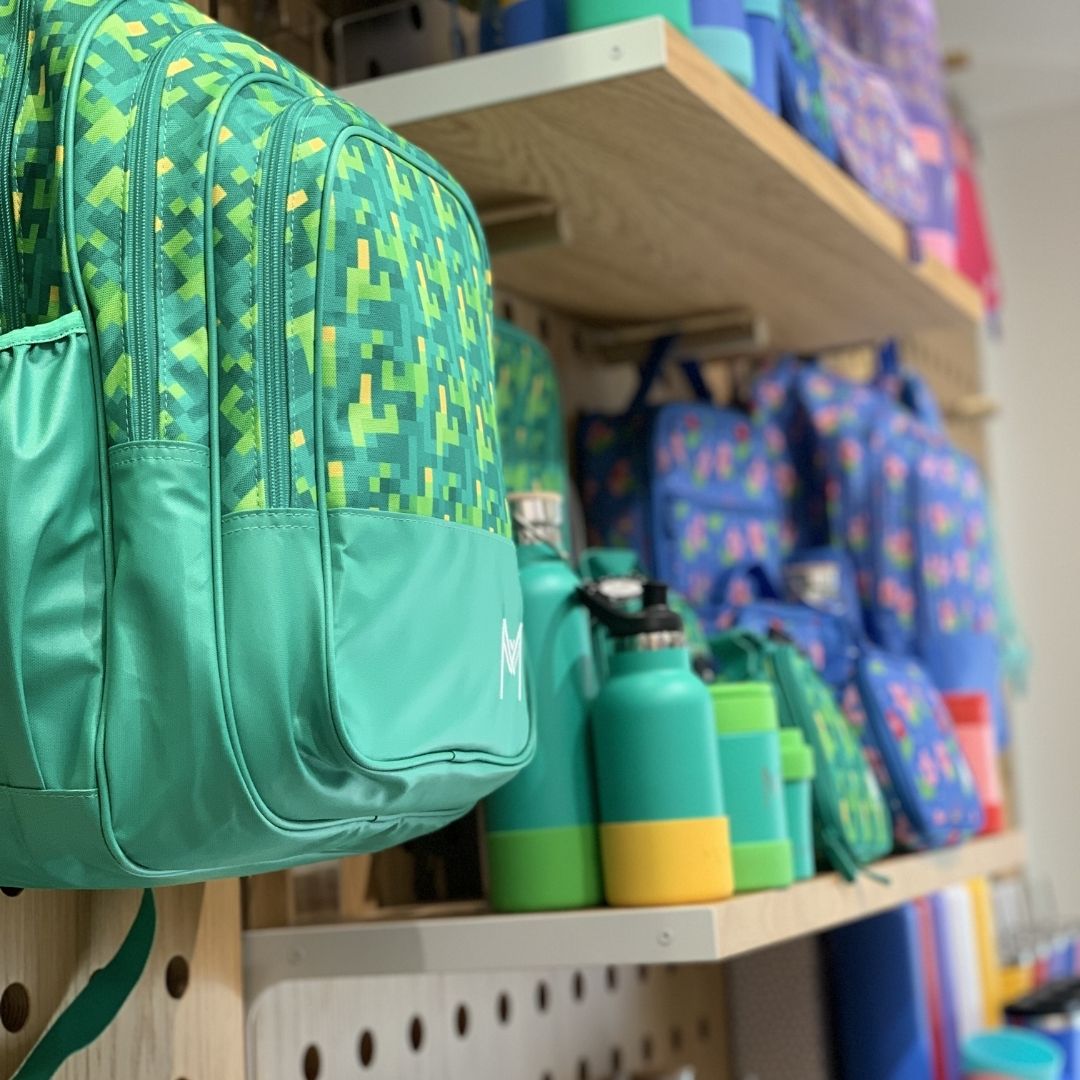 A close up of a MontiiCo Back Pack - Pixels handing off a wall with other MontiiCo products in the background on shelves.
