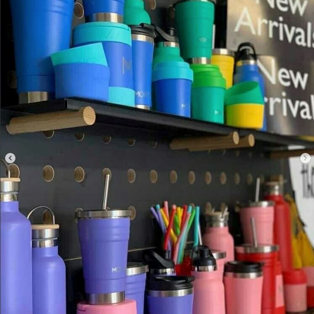 A mix of MontiiCo drink bottles, coffee cups, smoothie cups, bumpers and straws in a stockist store, on shelves.