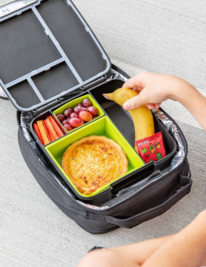 School Lunch box with compartments containing a pizza, fruits, and vegetables on a light gray surface.