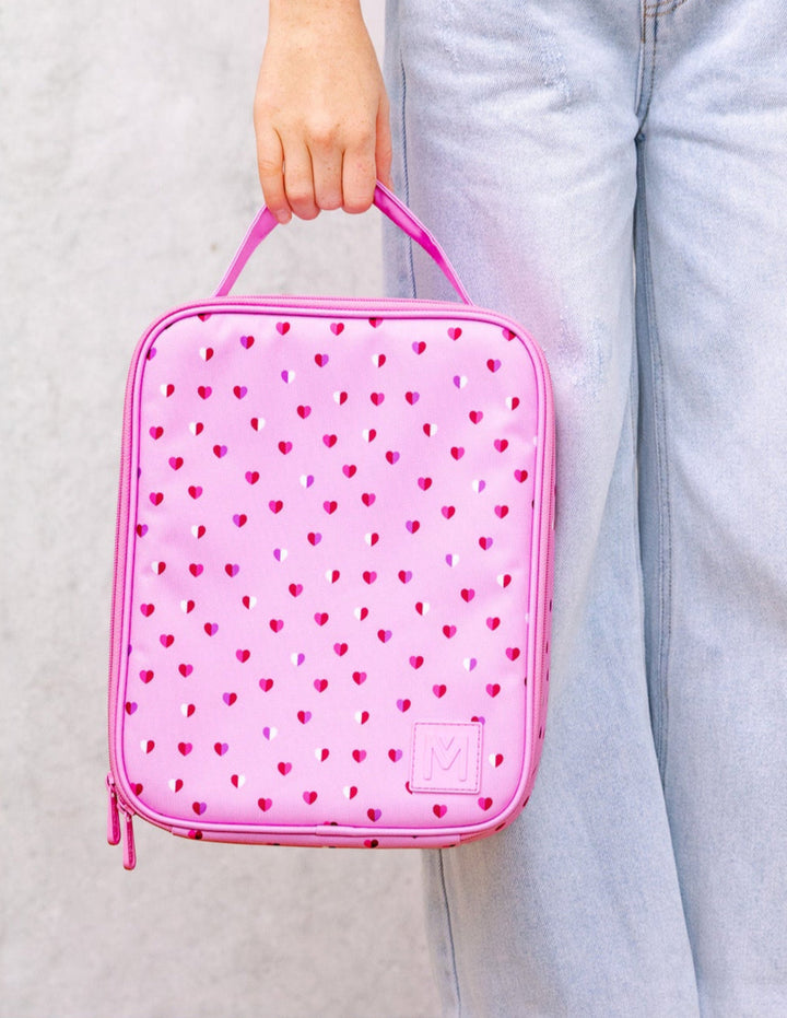 Pink heart-patterned insulated lunch bag held by a person wearing light blue jeans.