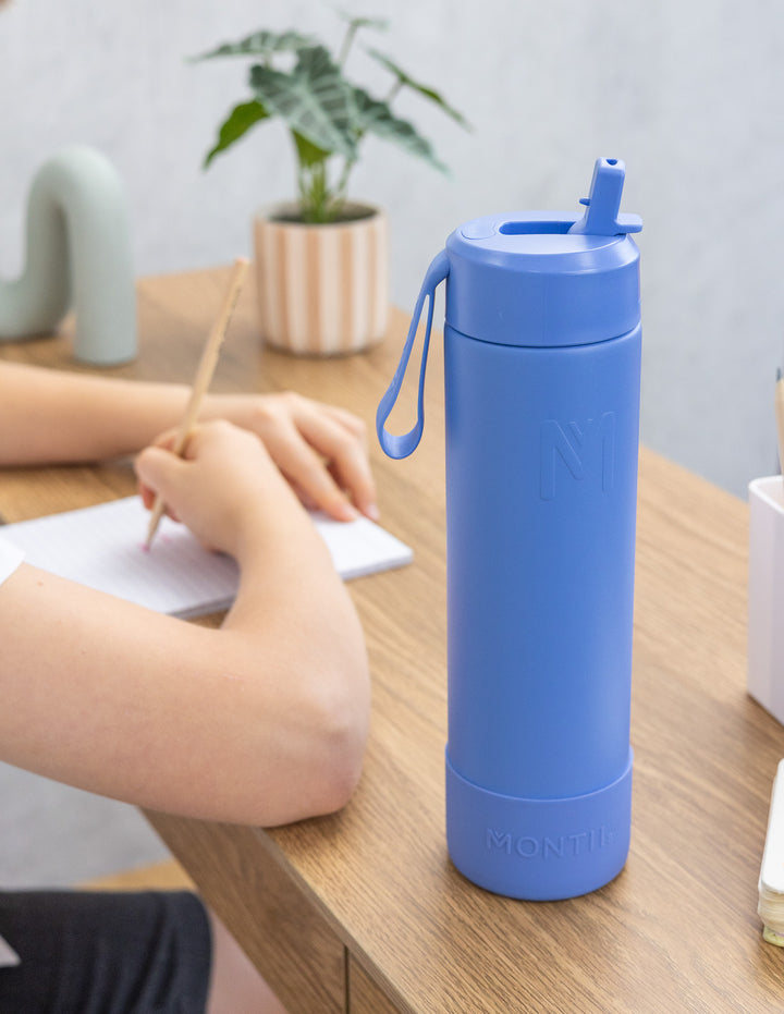 Blue water bottle on a desk with a person writing in the background