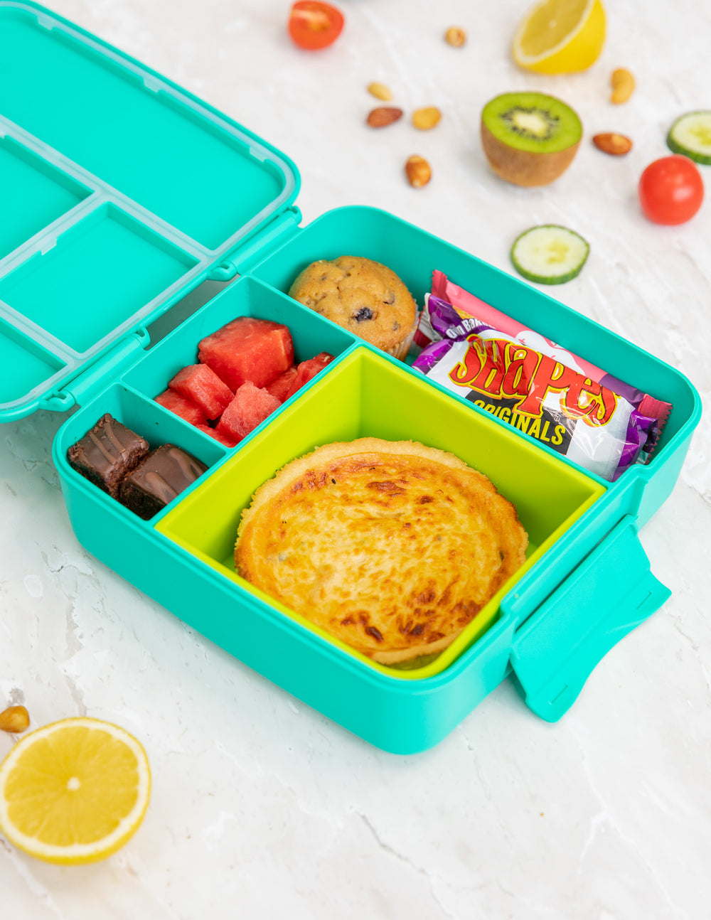 Colourful bento lunch box with various food items on a white background