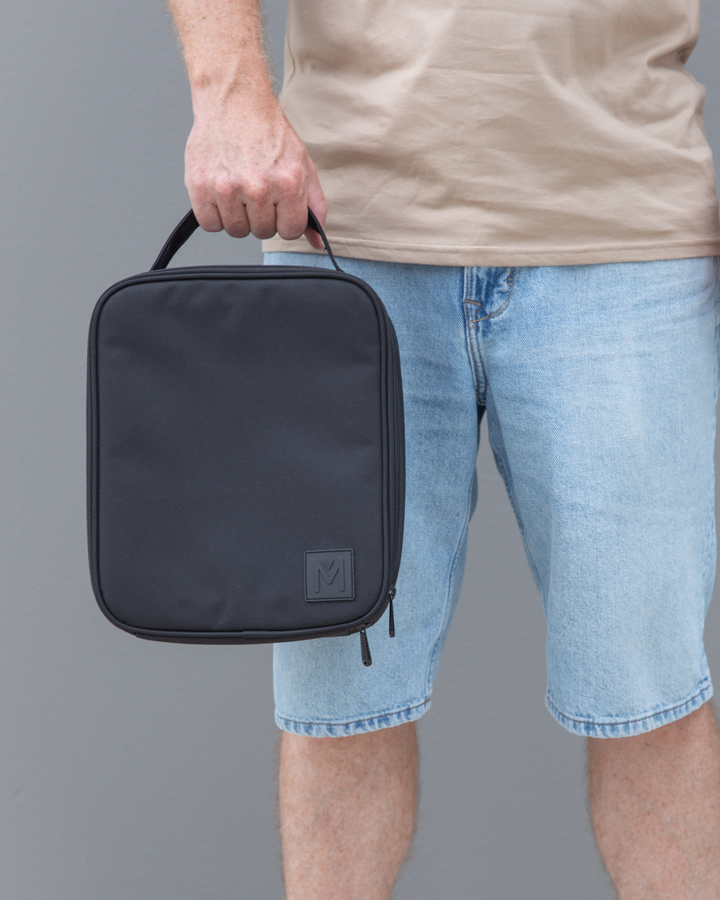 Person holding a black insulated lunch bag against a gray background