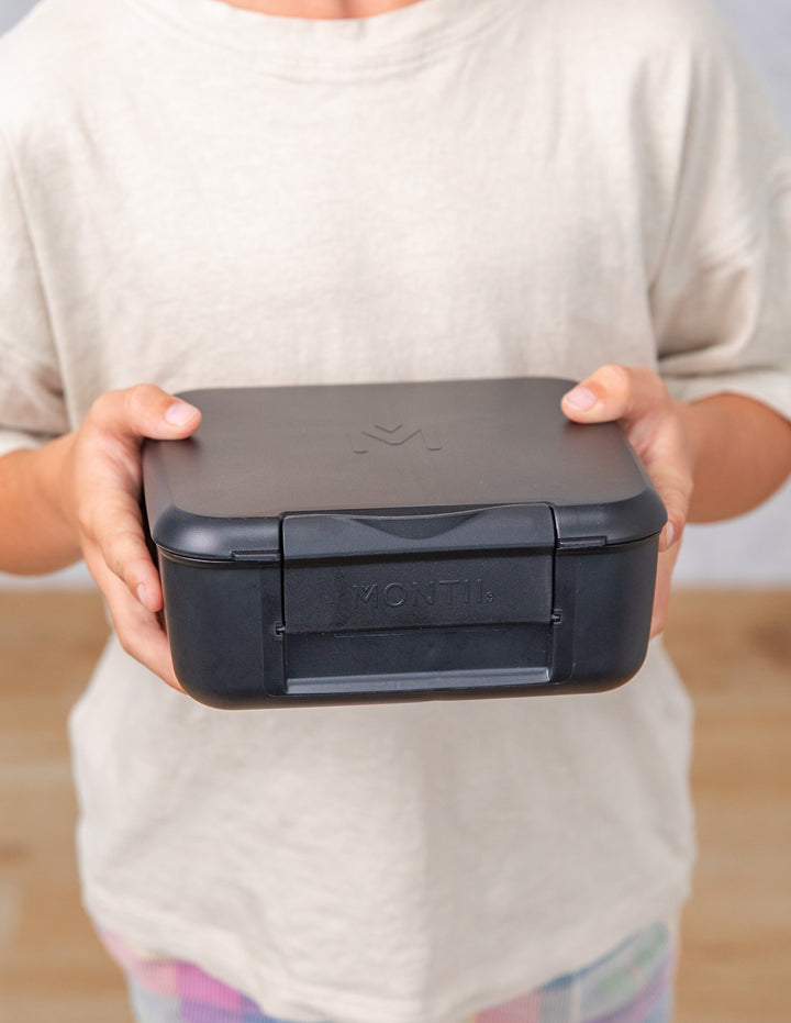 Person holding a black lunch box with a visible brand logo.