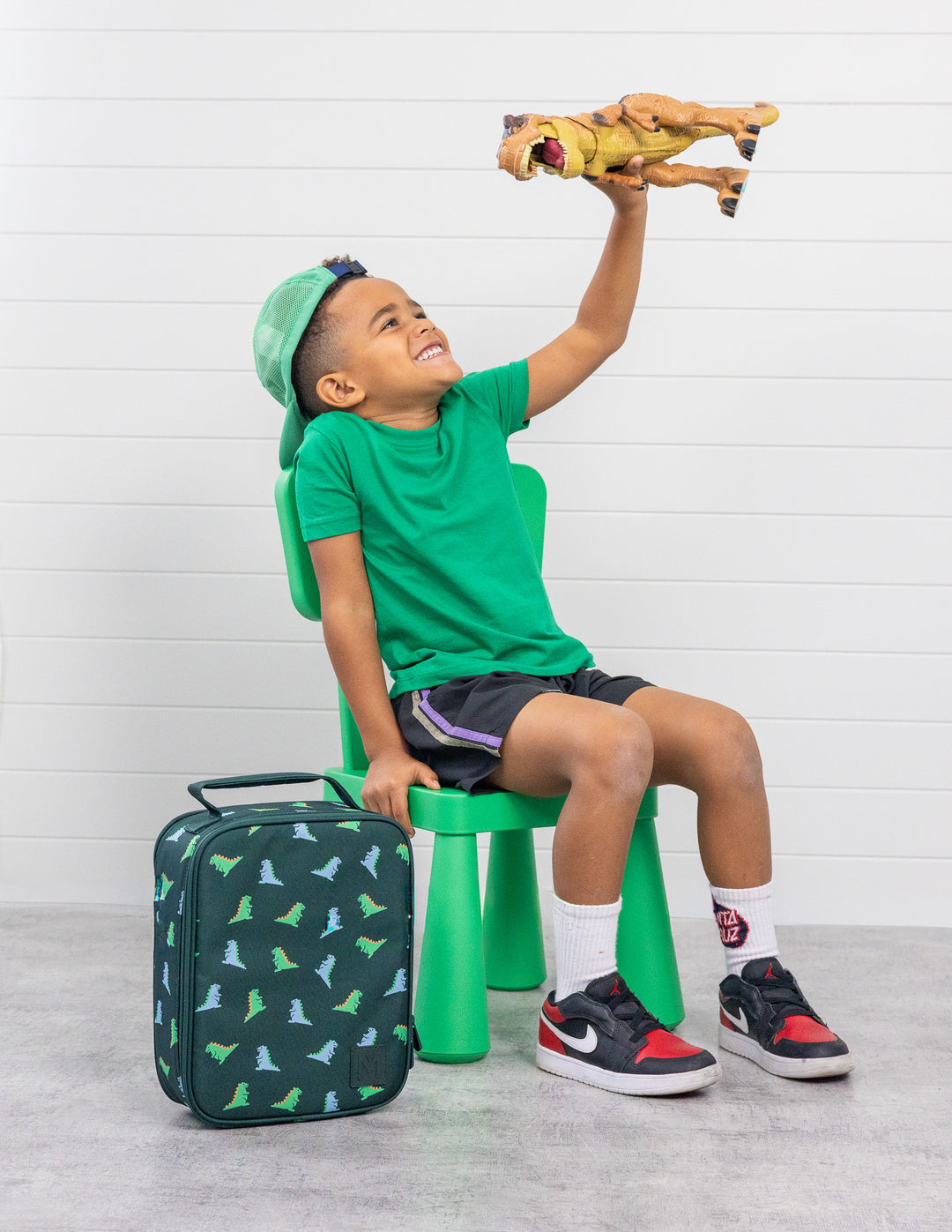 MontiiCo Large Lunch Bag - Dinosaur placed beside the kid 
