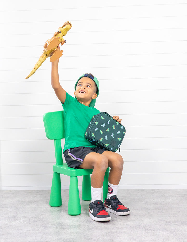 MontiiCo Medium Lunch Bag - Dinosaur child holding the bag sitting